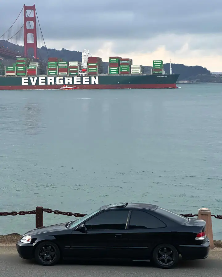 Black Honda Civic coupe parked by the bay with a container ship and the Golden Gate Bridge behind